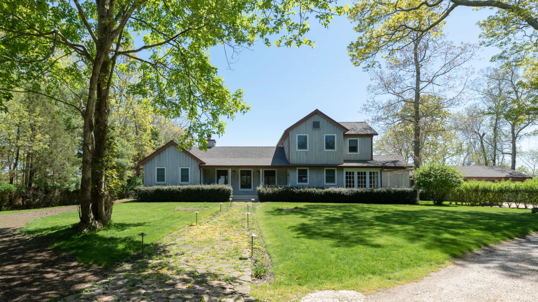 A large house stands beyond a broad lawn, framed by mature trees.