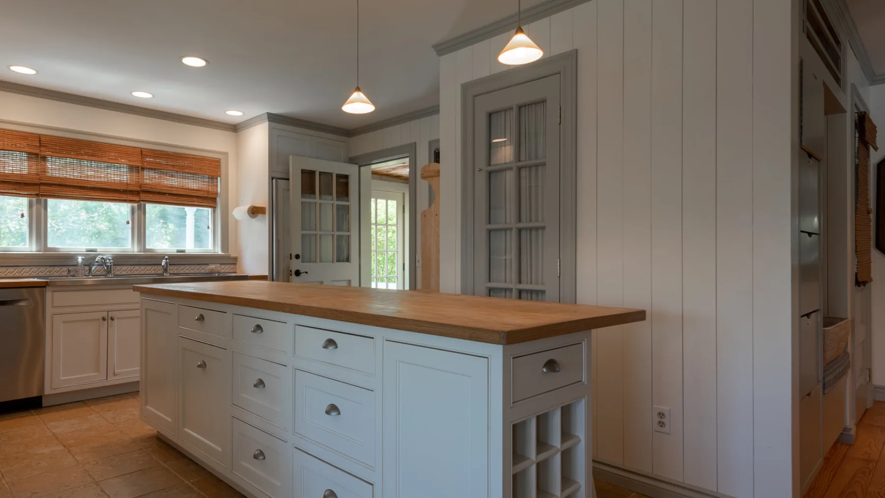 A bright kitchen with a large island, wooden countertop, and white cabinetry.