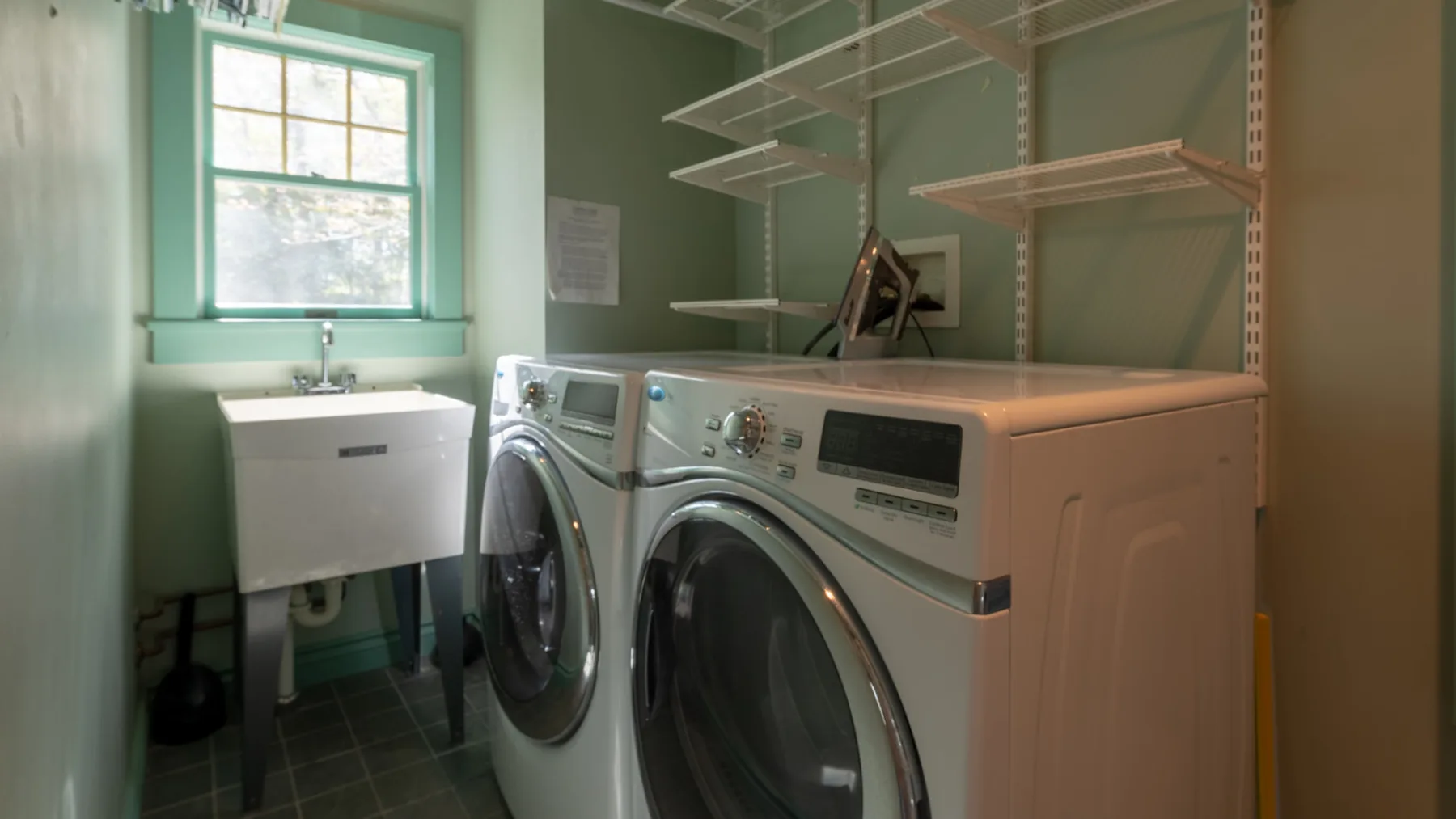 A laundry room with a washer and dryer beneath wall-mounted shelves.