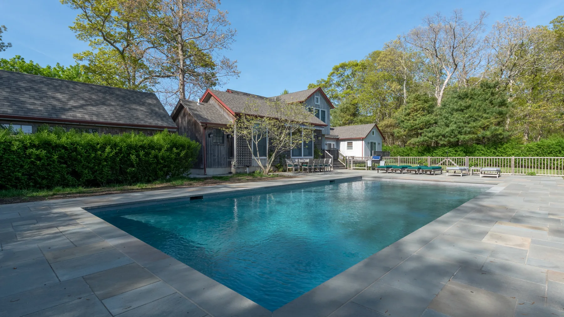An outdoor swimming pool sits beside a house and a paved patio.
