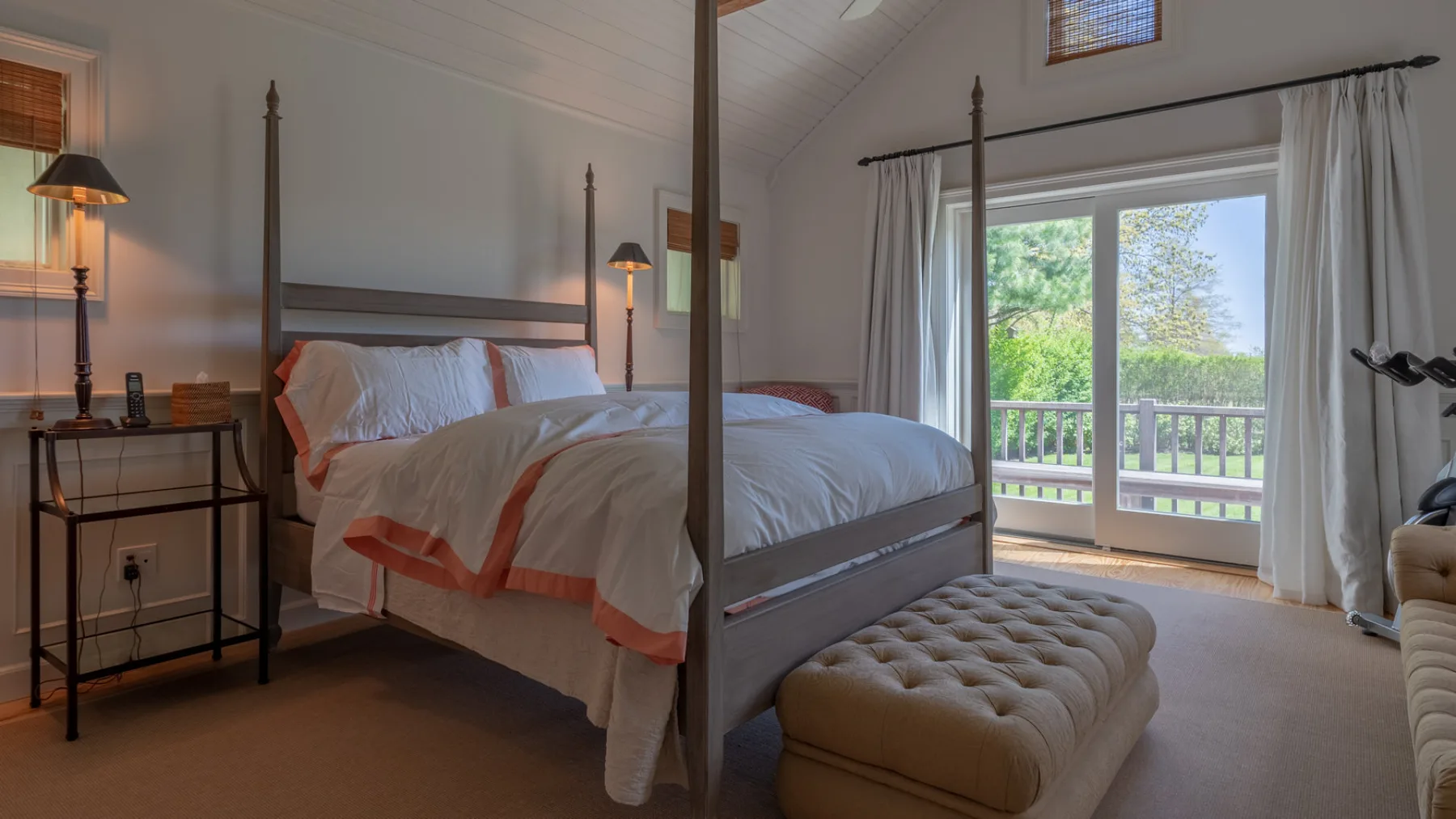 A bedroom with a large bed, an upholstered bench, and a glass door opening to a balcony.