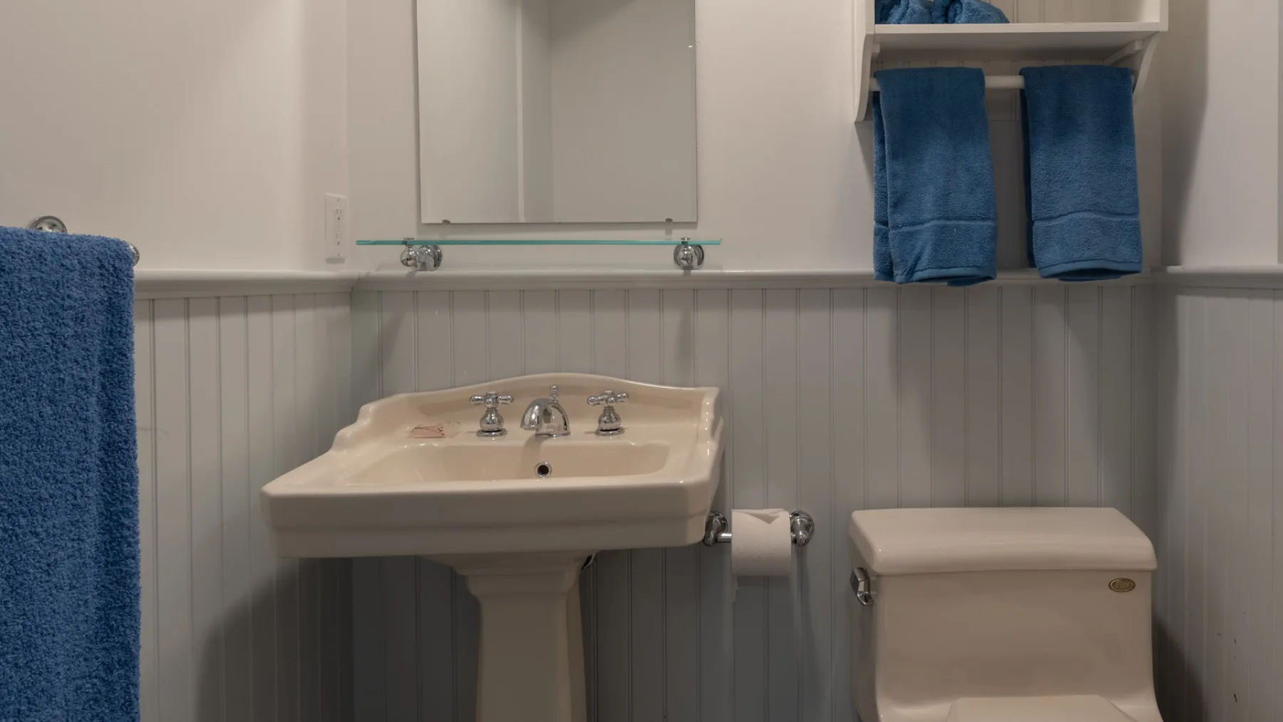 A bathroom vanity and toilet stand against pale paneled walls with blue towels.