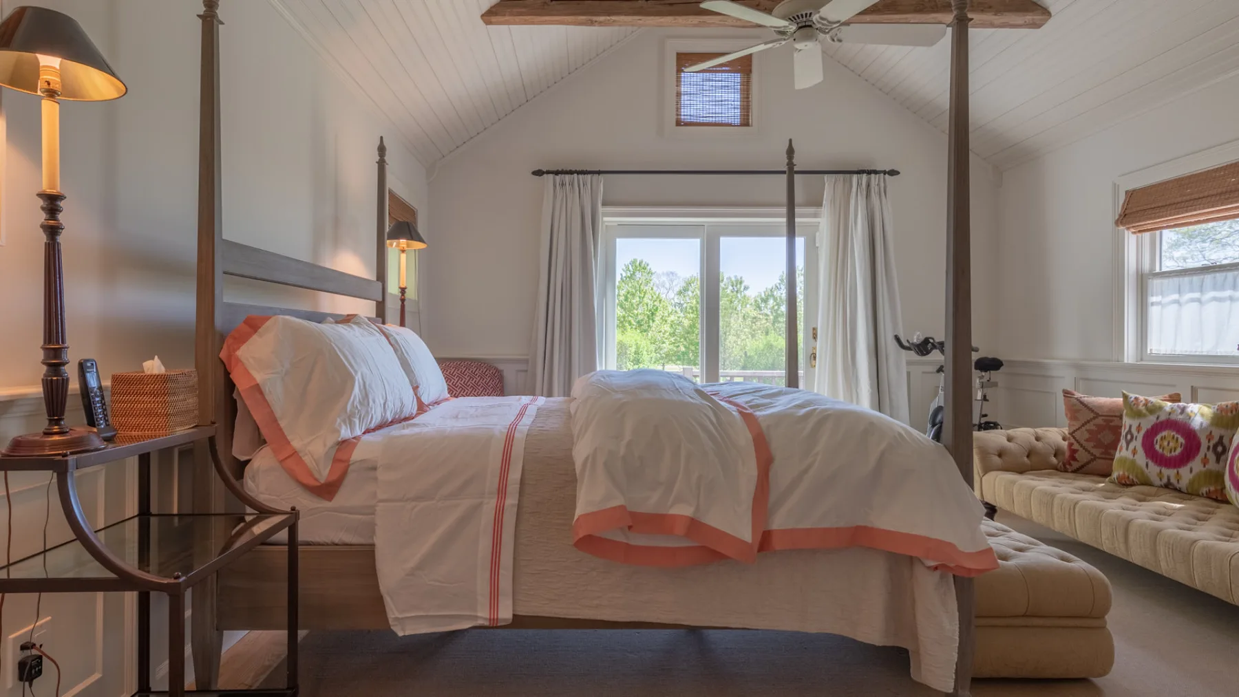 A bedroom with a canopy bed, bedside table, and seating by the window.