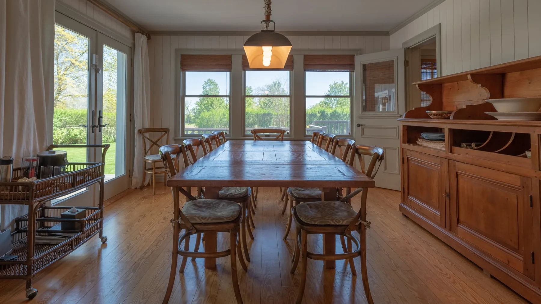 A dining room with a long wooden table and large windows.