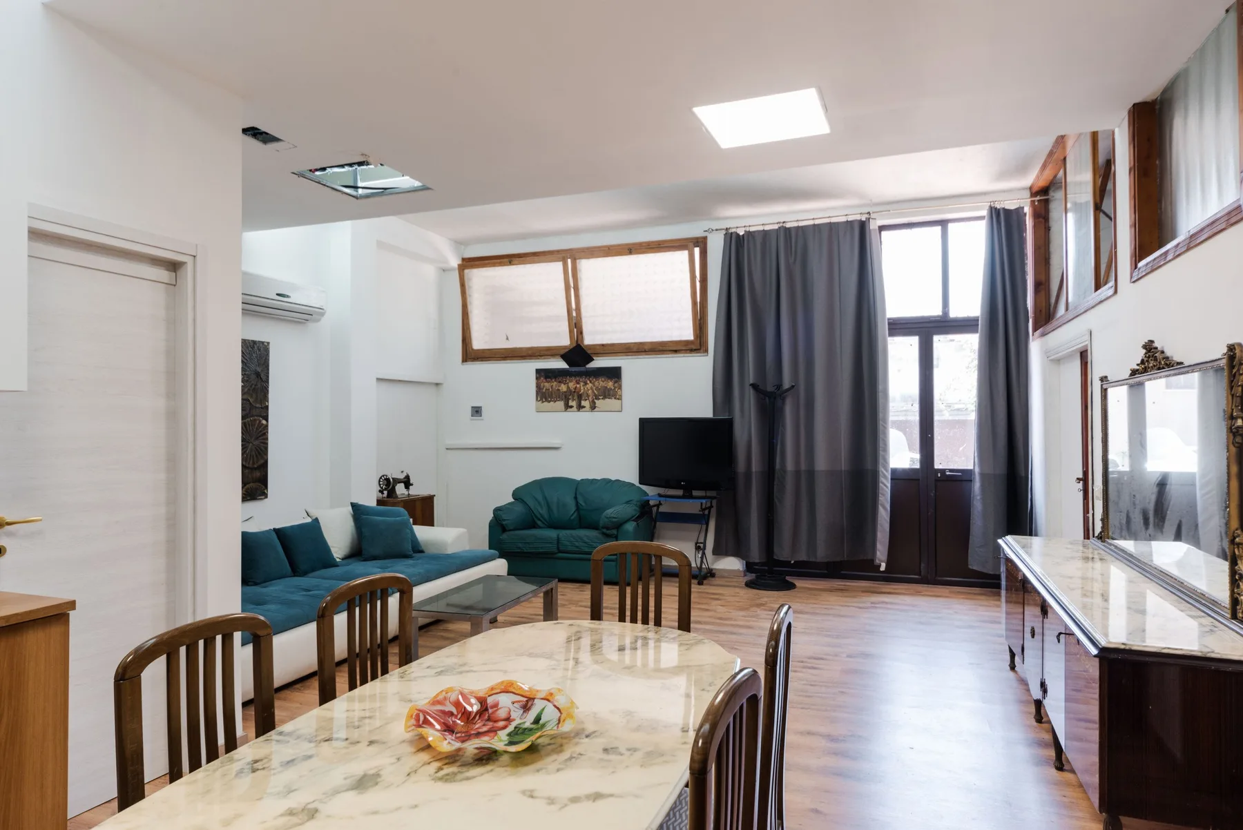 Una sala de estar y comedor con asientos, una mesa y ventanas altas.