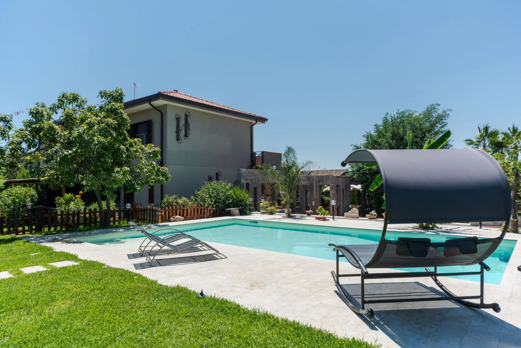 Una piscina exterior está junto al césped, con un asiento de descanso sombreado cerca.