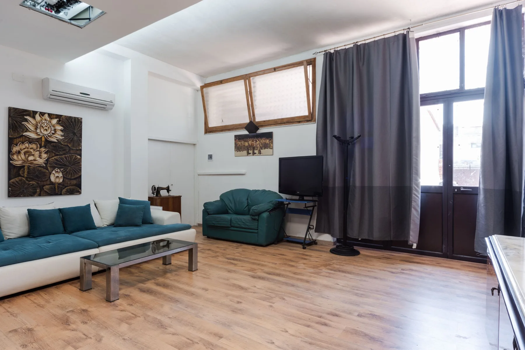 Una sala de estar con asientos color turquesa, un televisor y grandes ventanas con cortinas.