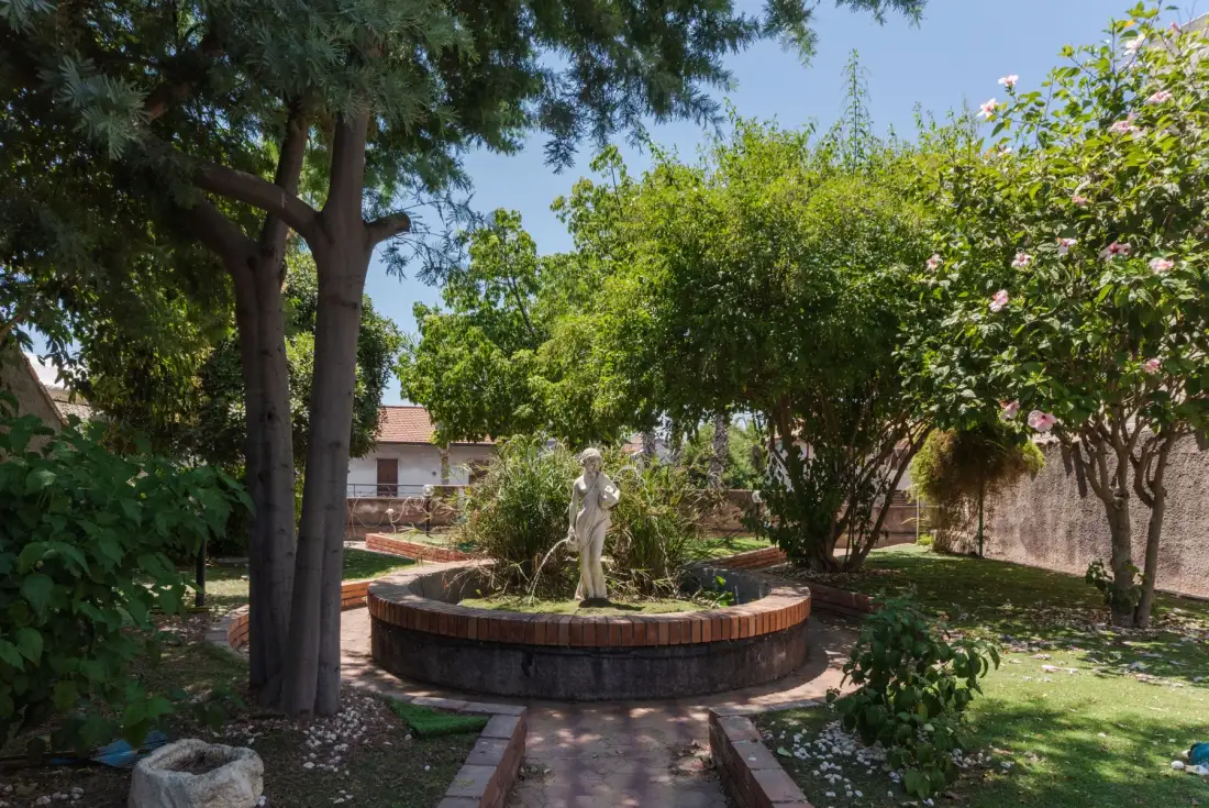 Un patio ajardinado con una fuente circular rodeada de árboles y arbustos en flor.