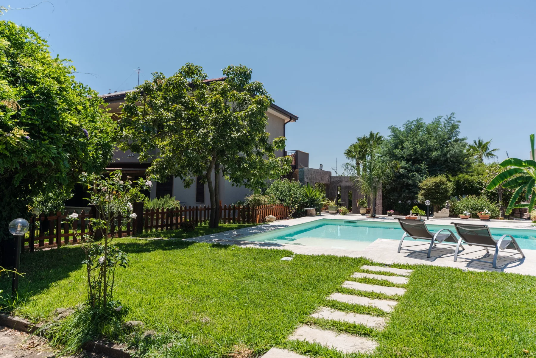 Una piscina en el patio está junto a un césped y árboles frondosos.
