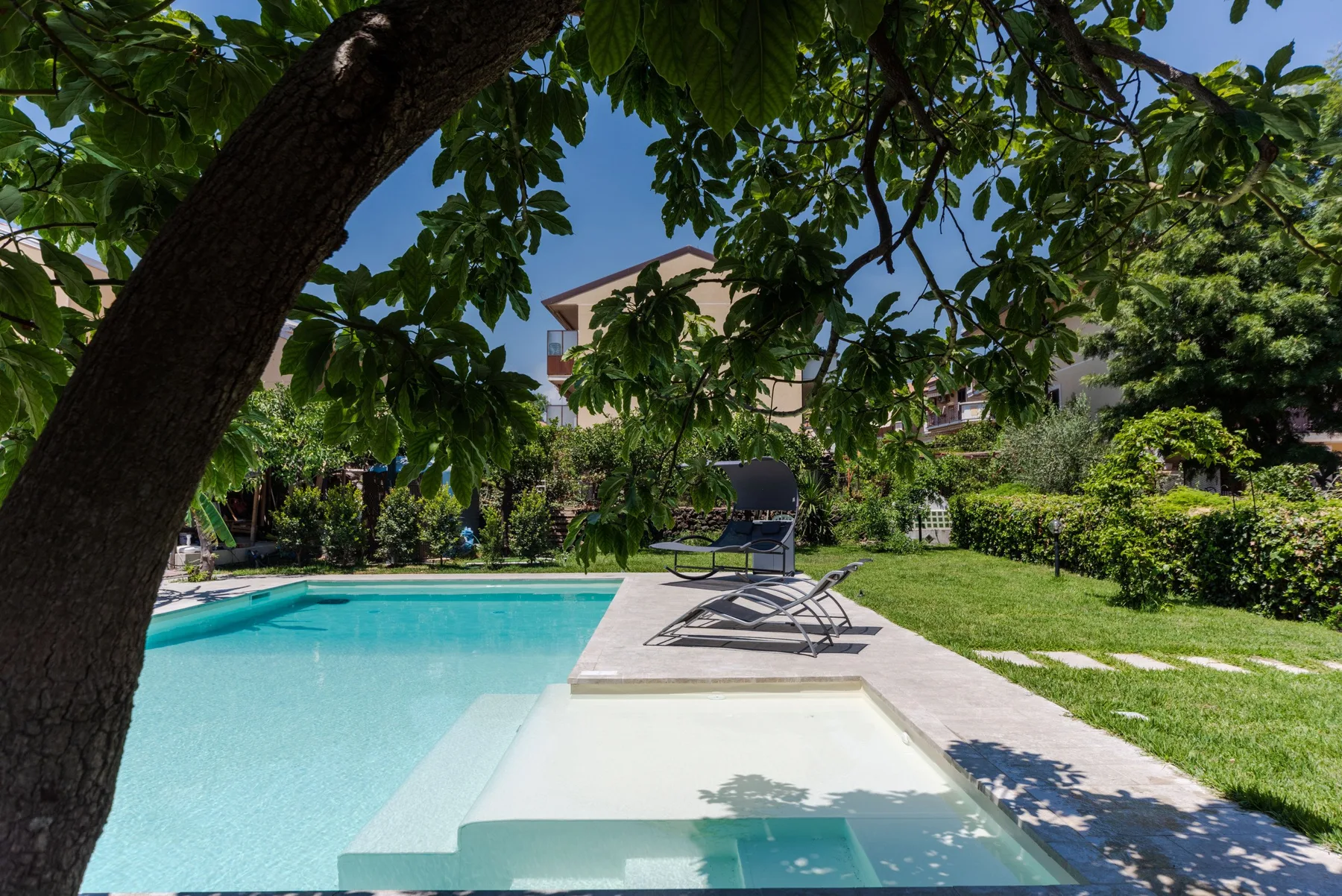 Piscina al aire libre junto a un jardín con césped y asientos en la terraza.