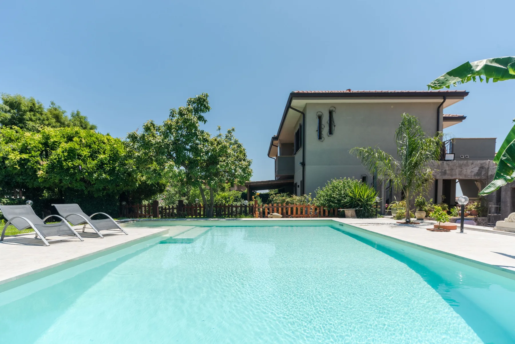 Una piscina al aire libre está junto a una casa, con asientos para descansar en el borde.