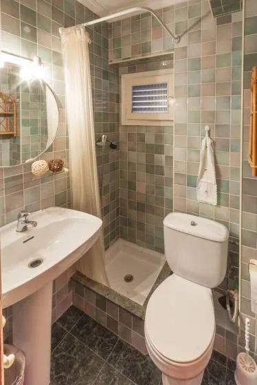 A tiled bathroom with a sink, toilet, and shower behind a curtain.