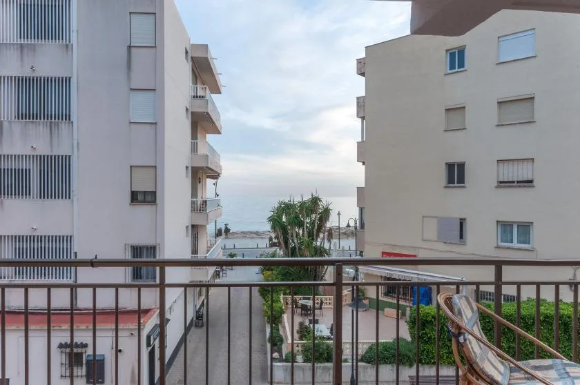 A balcony overlooks nearby buildings, palm trees, and the sea.