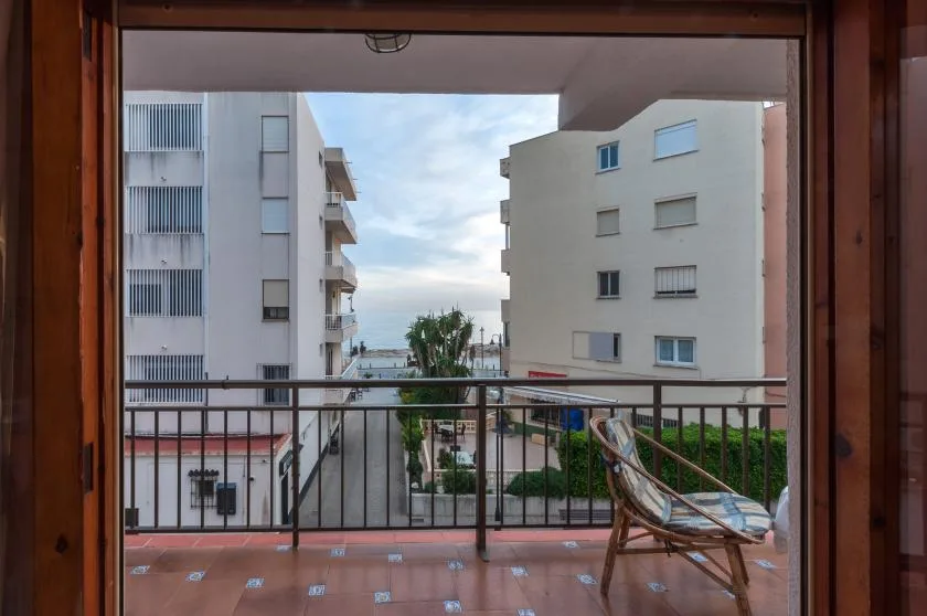 A balcony overlooks nearby apartment buildings, with a chair beside the railing.