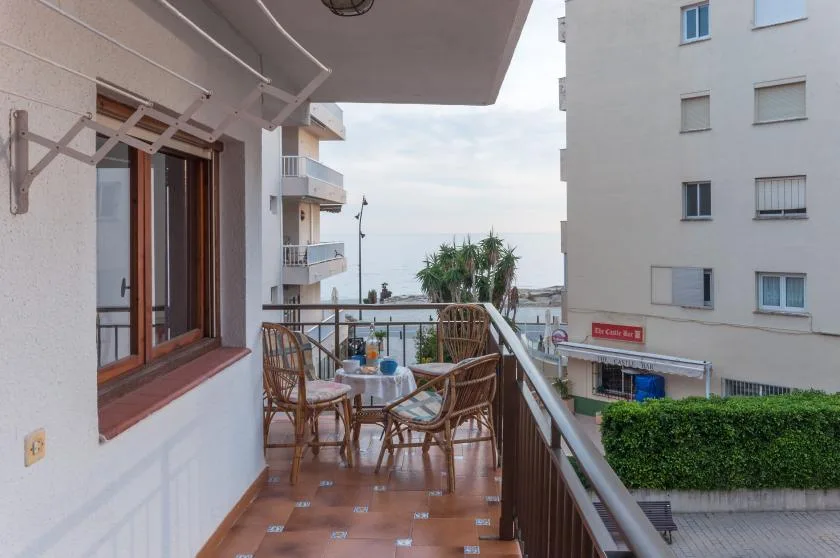 A balcony with outdoor seating overlooks nearby buildings and the sea.