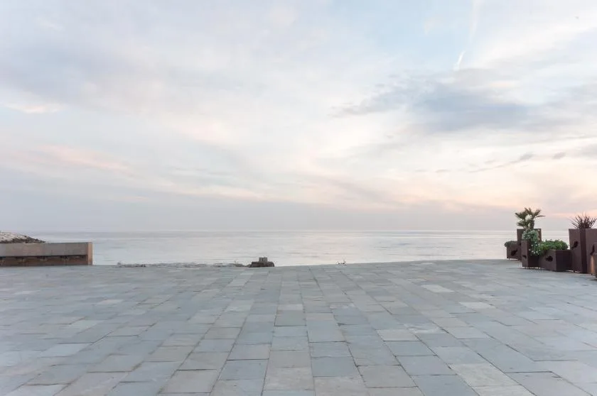 A tiled terrace opens onto a calm sea beneath a cloudy sky.