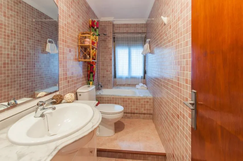 A tiled bathroom with a sink, toilet, and bathtub beneath a window.