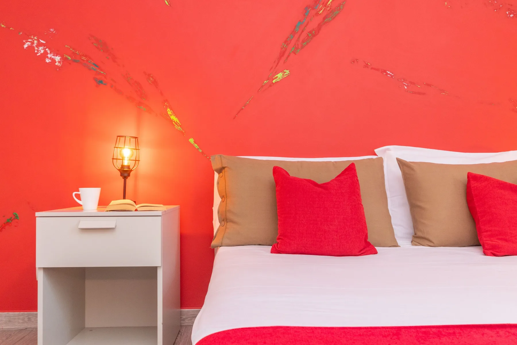 A bed with red and tan pillows sits against a bright red wall.