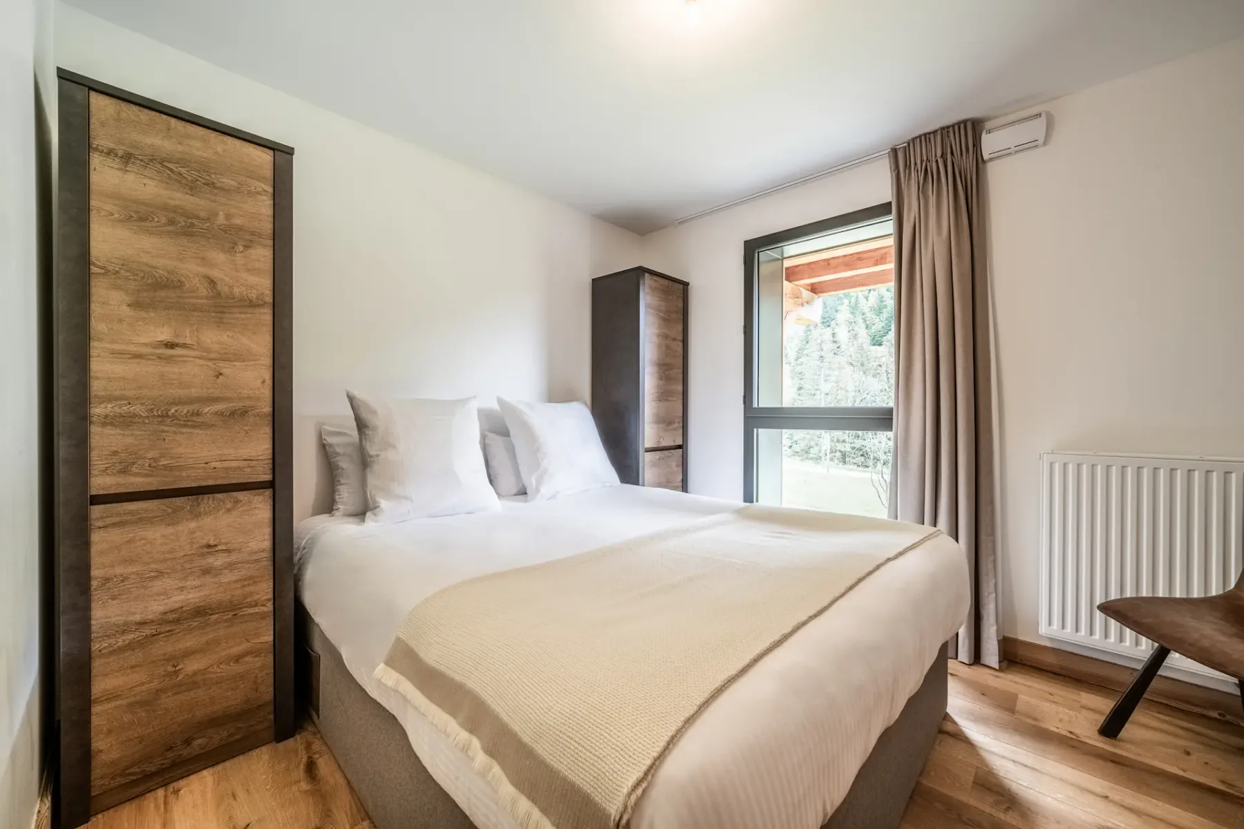 Un dormitorio con una cama, armarios, una ventana con cortinas y un radiador.