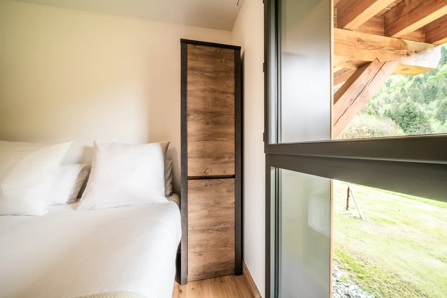 Un dormitorio con una cama junto a un armario alto de madera y una gran ventana de vidrio.