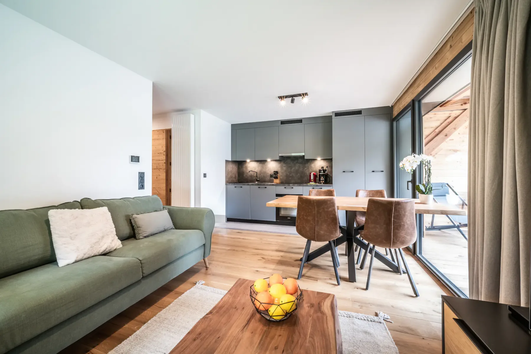 A living room and dining area with green seating, a coffee table, and large windows.