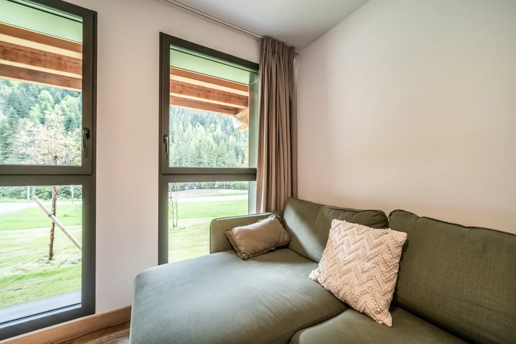 A living room with green seating beside large windows overlooking a grassy area.
