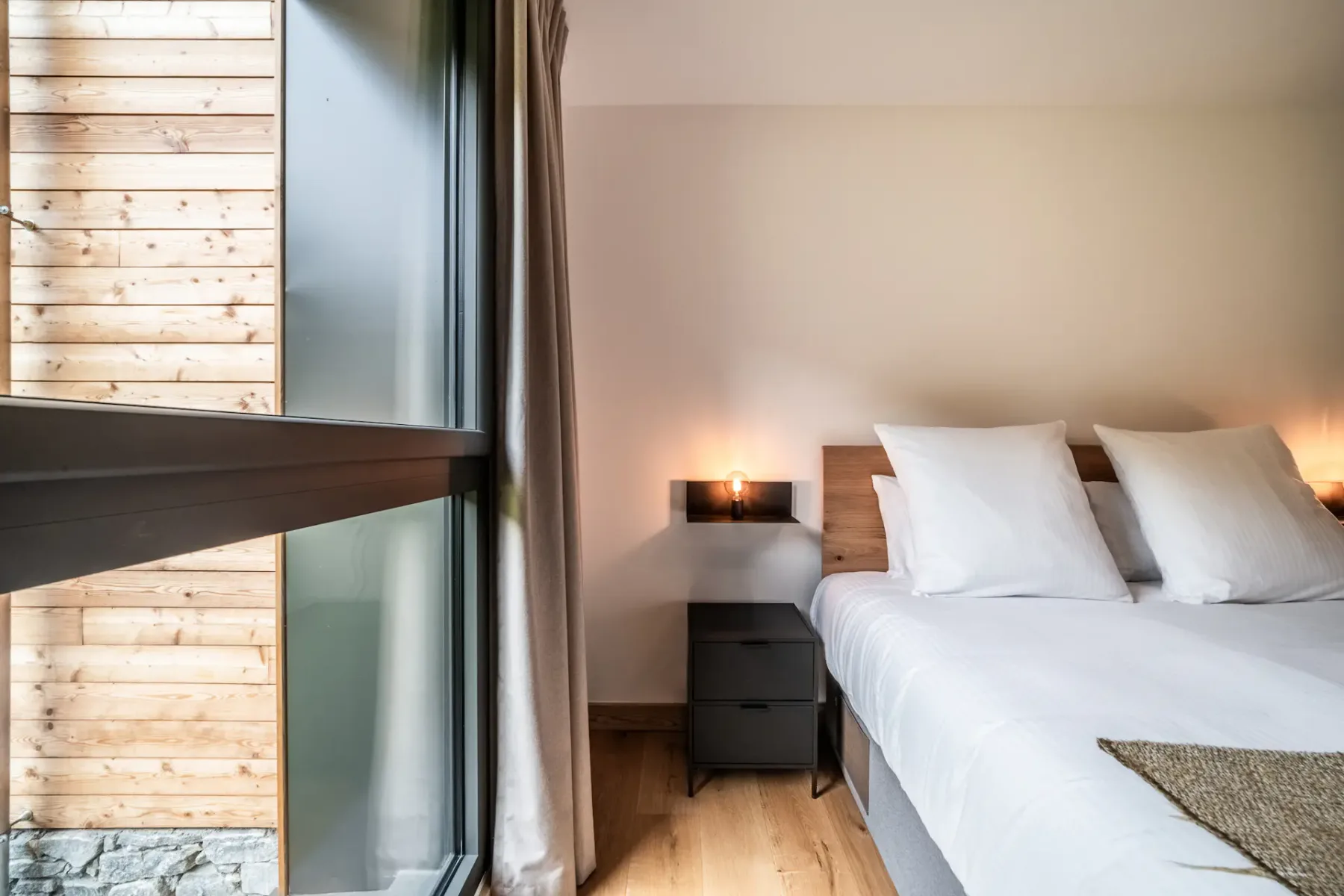 Un dormitorio bien ordenado con una cama grande, suelo de madera, mesas de noche, un armario con espejos y una ventana que aporta luz natural.