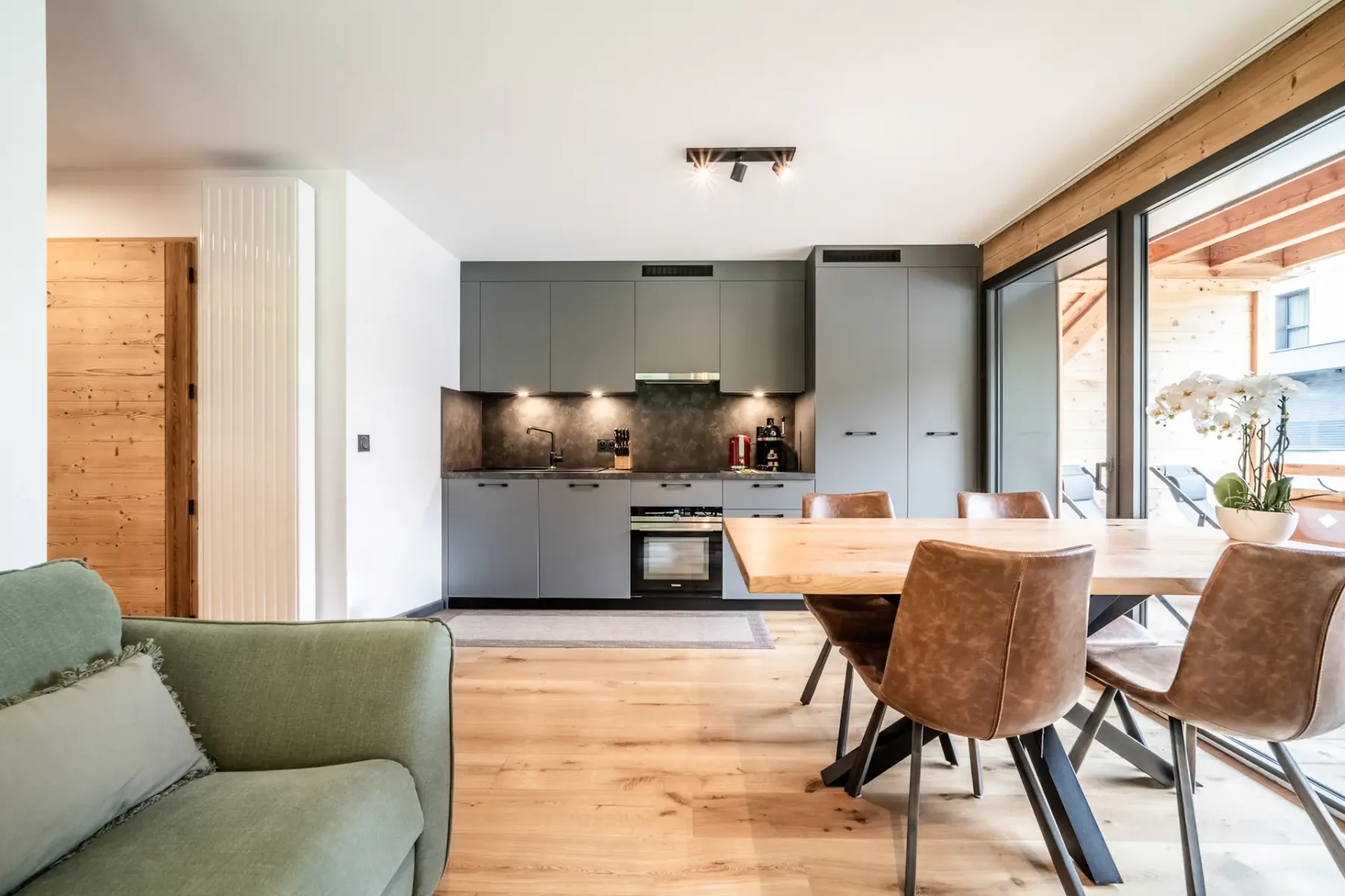 Una cocina se abre a un comedor, con armarios grises y un sofá verde en primer plano.