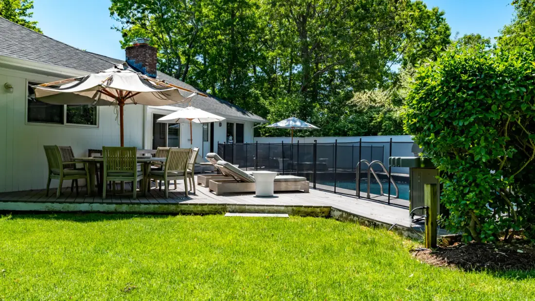Un patio trasero con asientos al aire libre, sombrillas y una piscina.