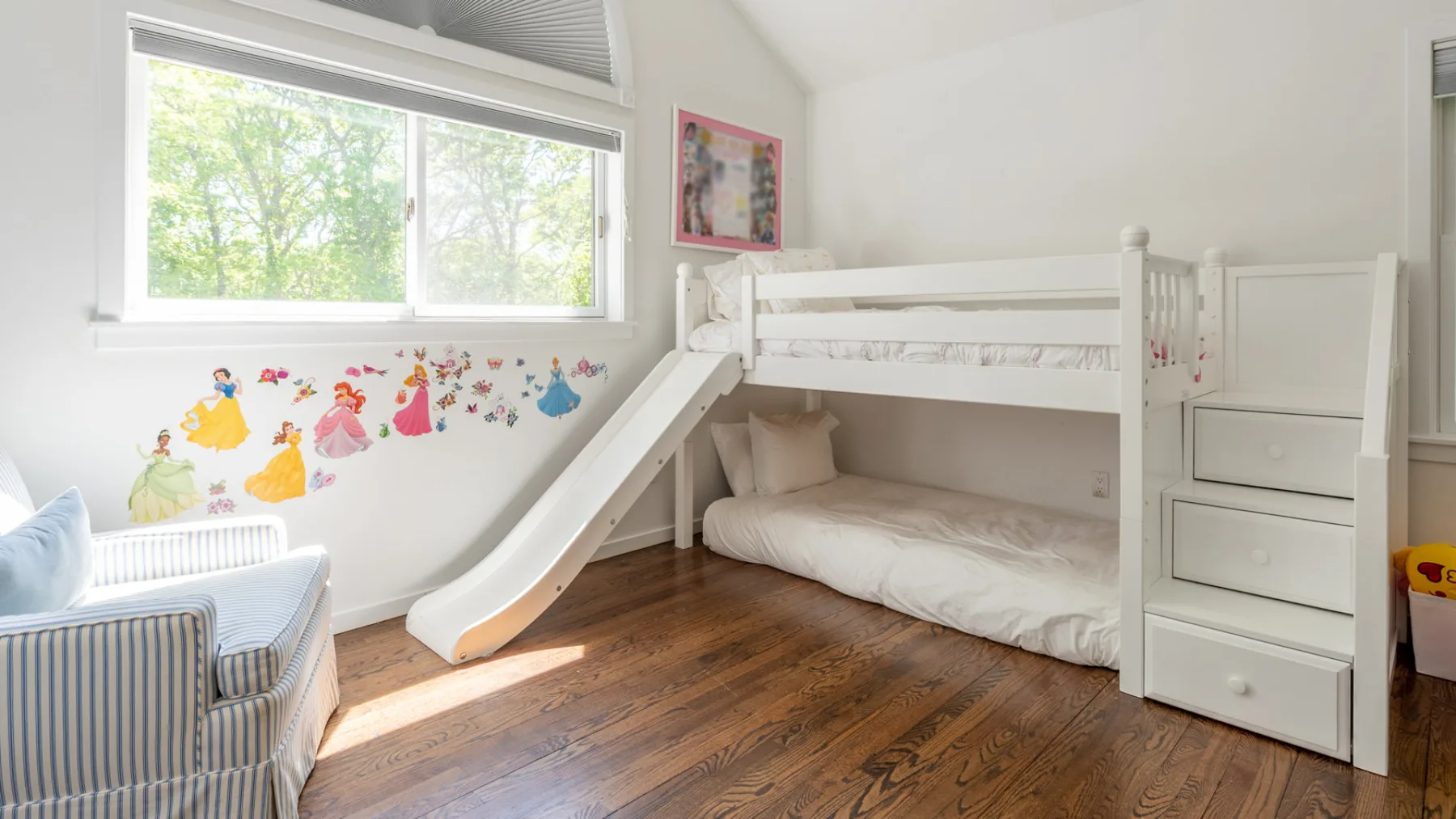 Dormitorio infantil con litera blanca, tobogán y coloridos adhesivos en la pared.