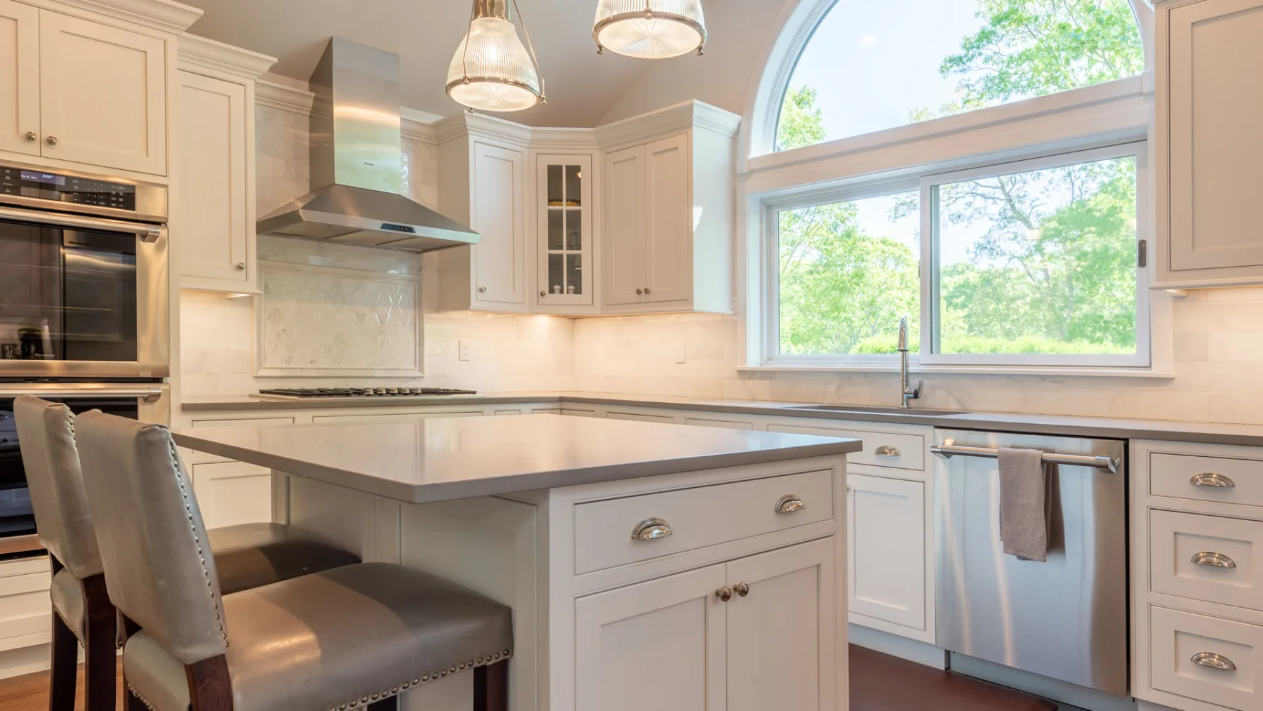Una cocina luminosa con una isla central, gabinetes blancos y ventanas grandes.