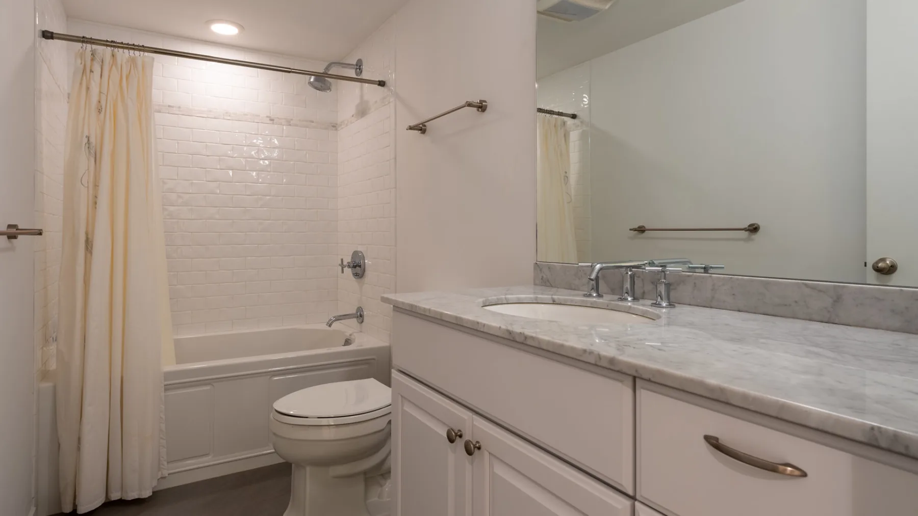 Un baño con bañera, inodoro y lavabo bajo un espejo grande.