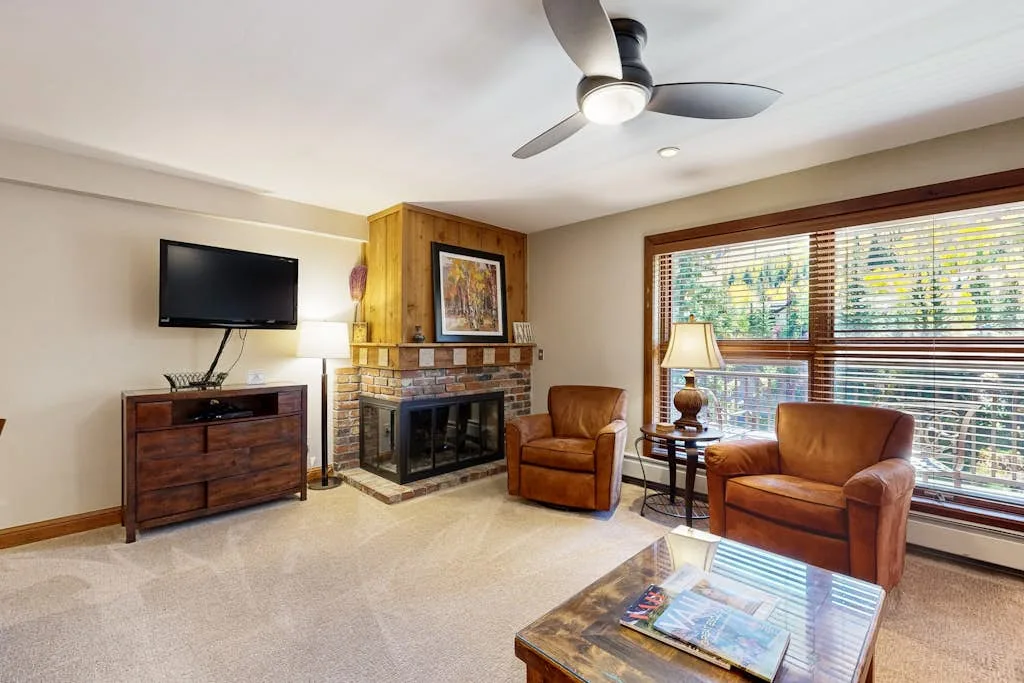 A living room with armchairs, a fireplace, and large windows.