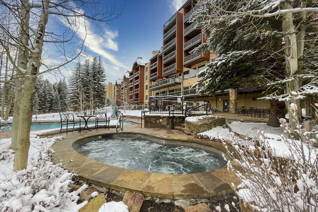 An outdoor pool and hot tub sit beside a multistory building in a snowy courtyard.