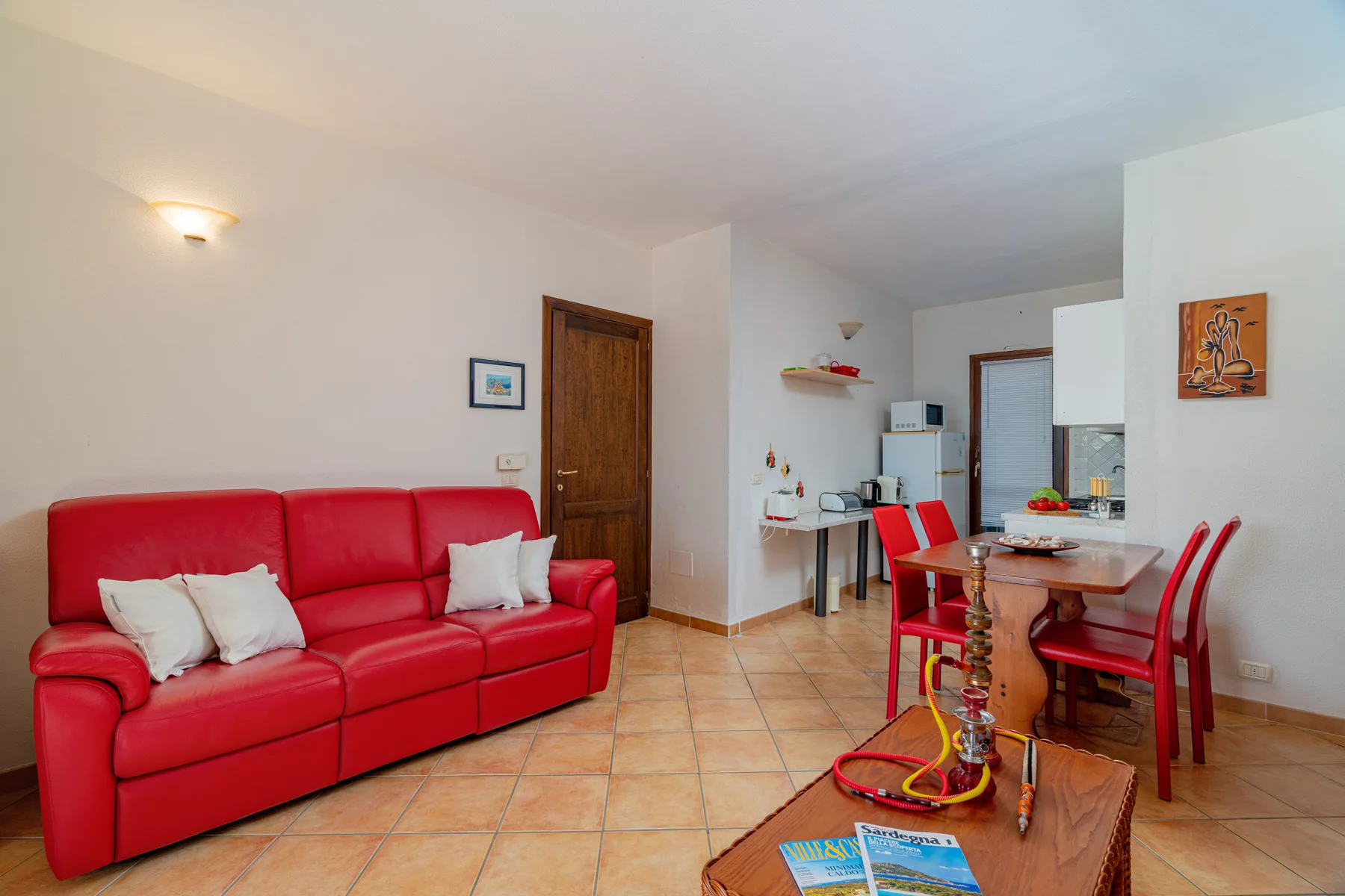 Una sala de estar y comedor cuenta con asientos rojos, una mesa de madera y piso de baldosas.
