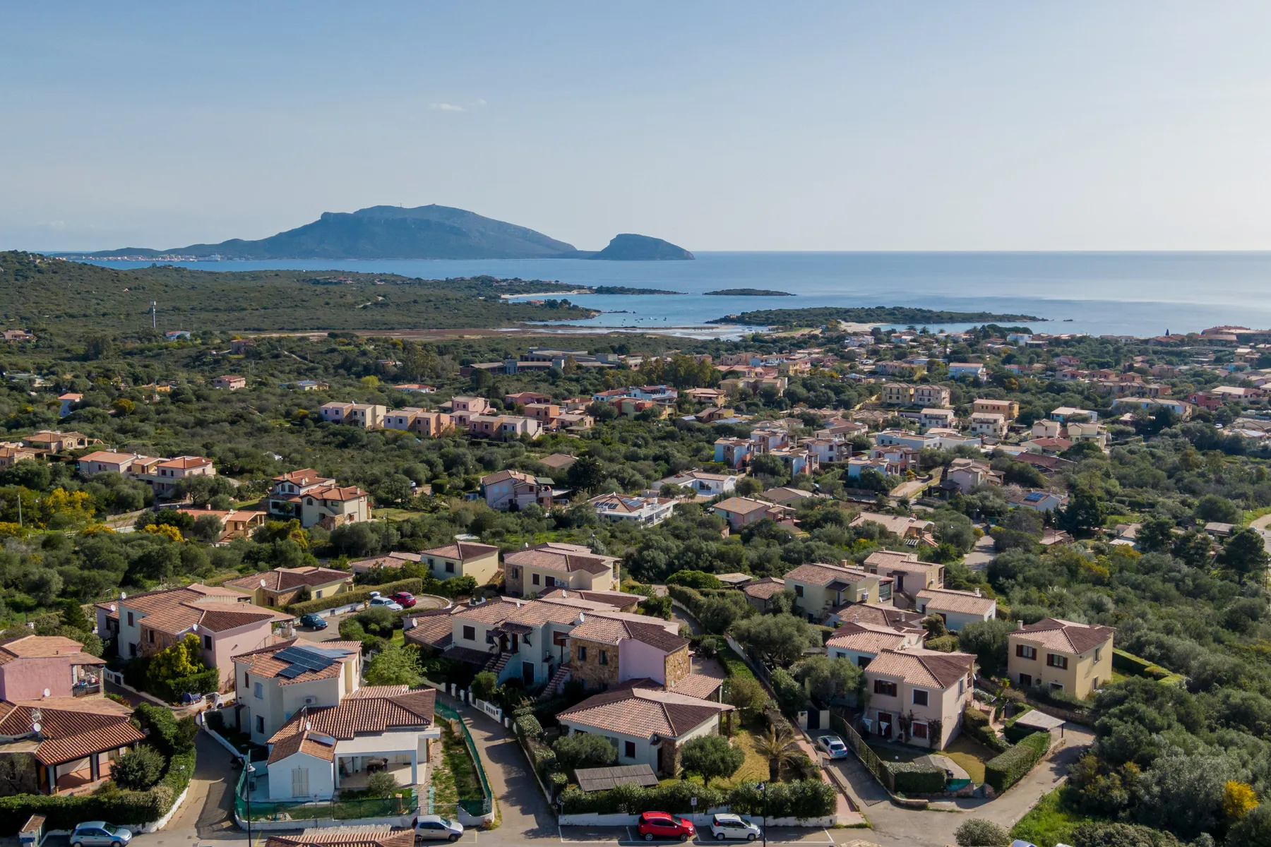 Vista aérea de un barrio costero con casas, vegetación y el mar al fondo.