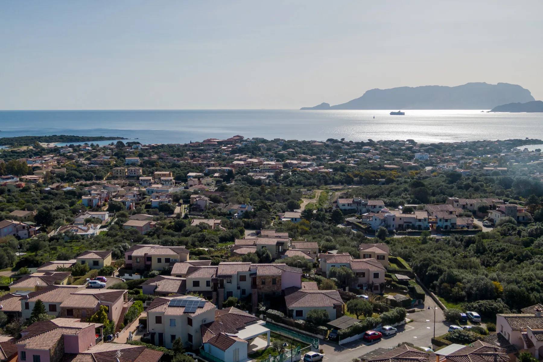 Vista aérea de un barrio costero con el mar y una isla a lo lejos.