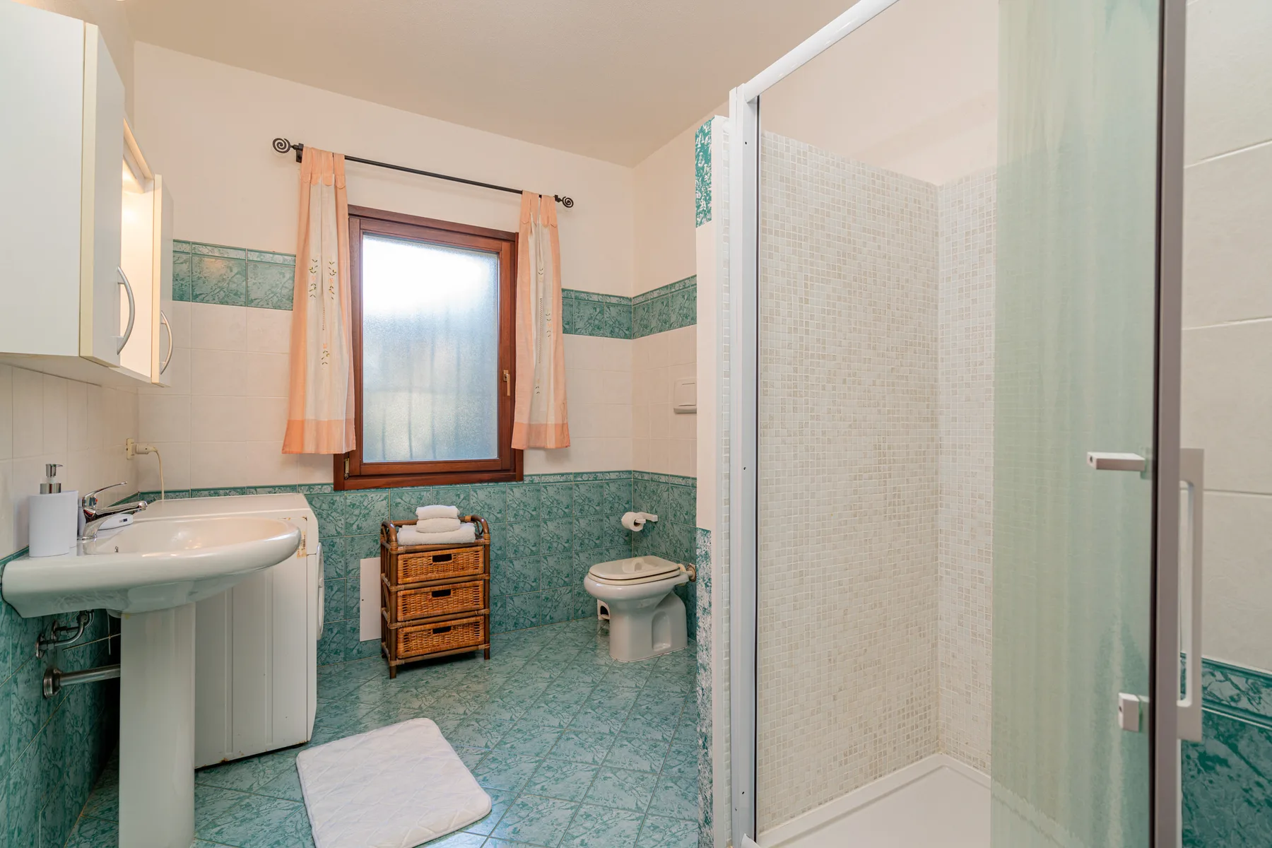 Un baño con azulejos, lavabo, inodoro, ducha y ventana.
