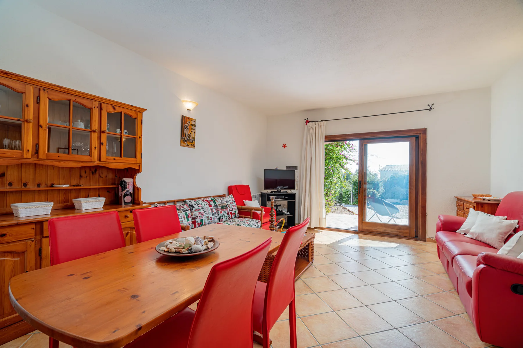 Una zona de comedor y estar con una mesa de madera y puertas corredizas de vidrio hacia un patio.