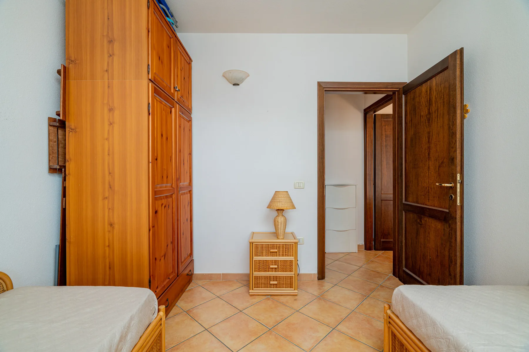 Un dormitorio con armarios de madera, una pequeña mesita y camas en los bordes de la imagen.