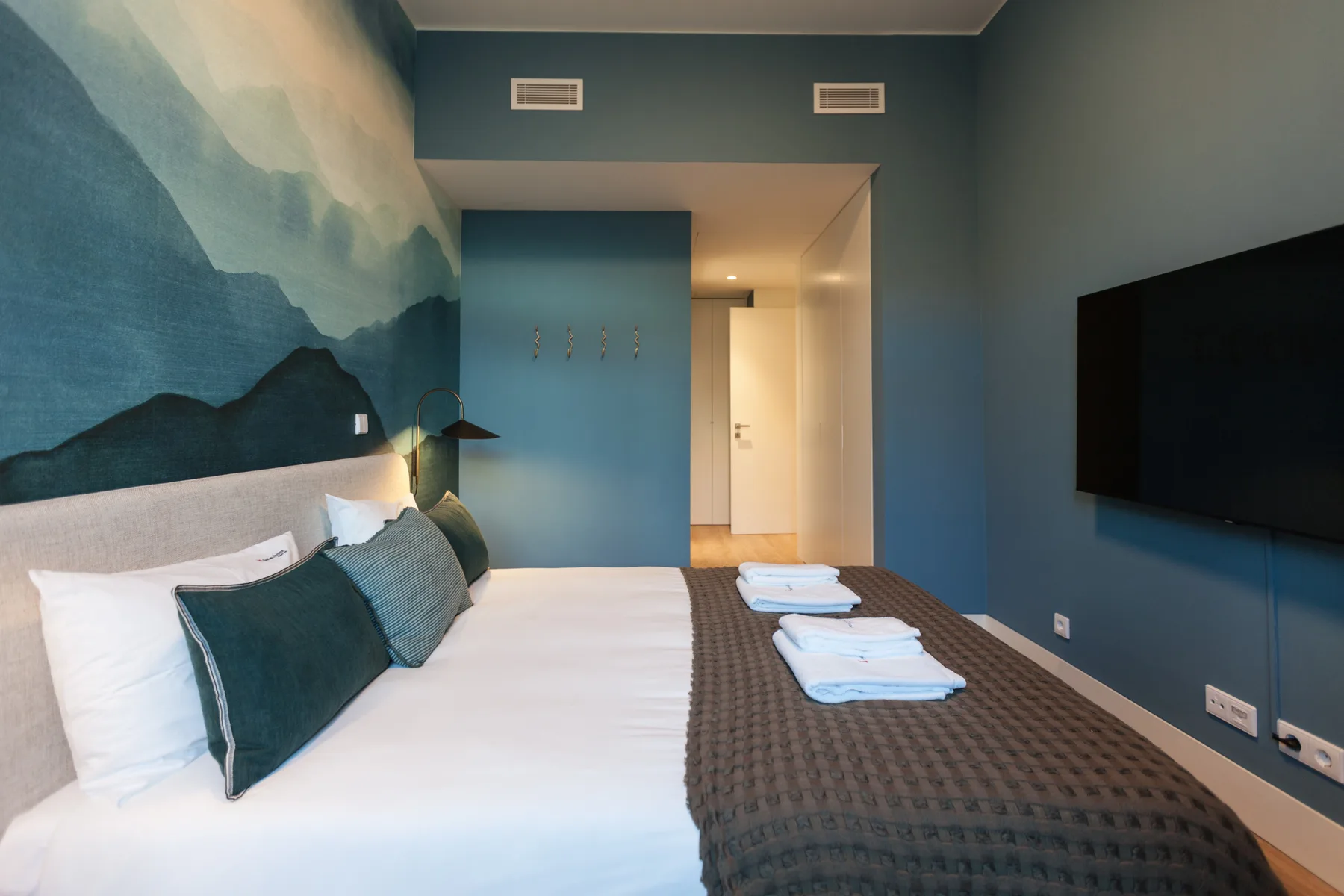 Un dormitorio con una cama, toallas dobladas y un televisor montado en la pared.