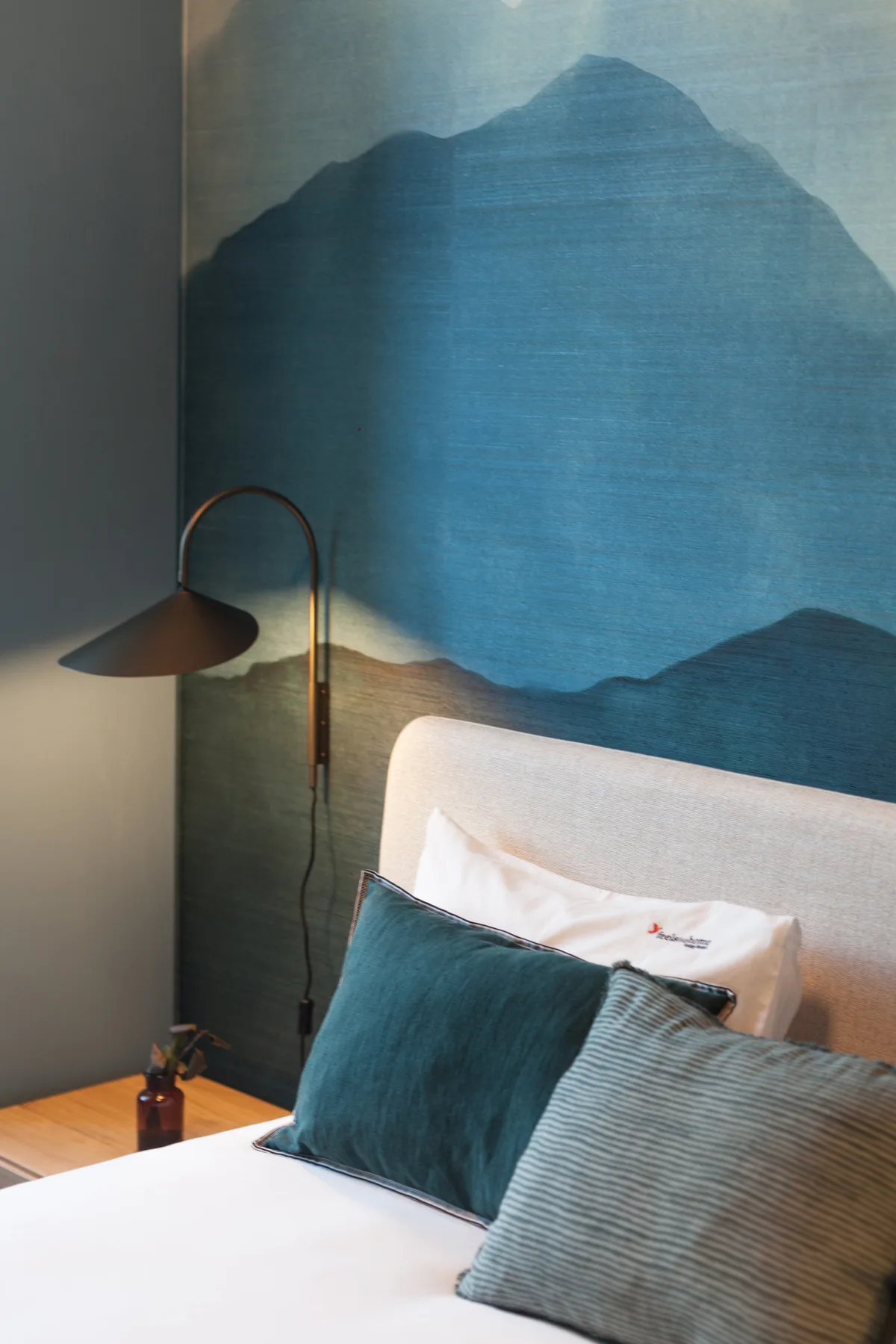 Un dormitorio con una cama, cojines decorativos y una lámpara de pie junto a un mural azul.