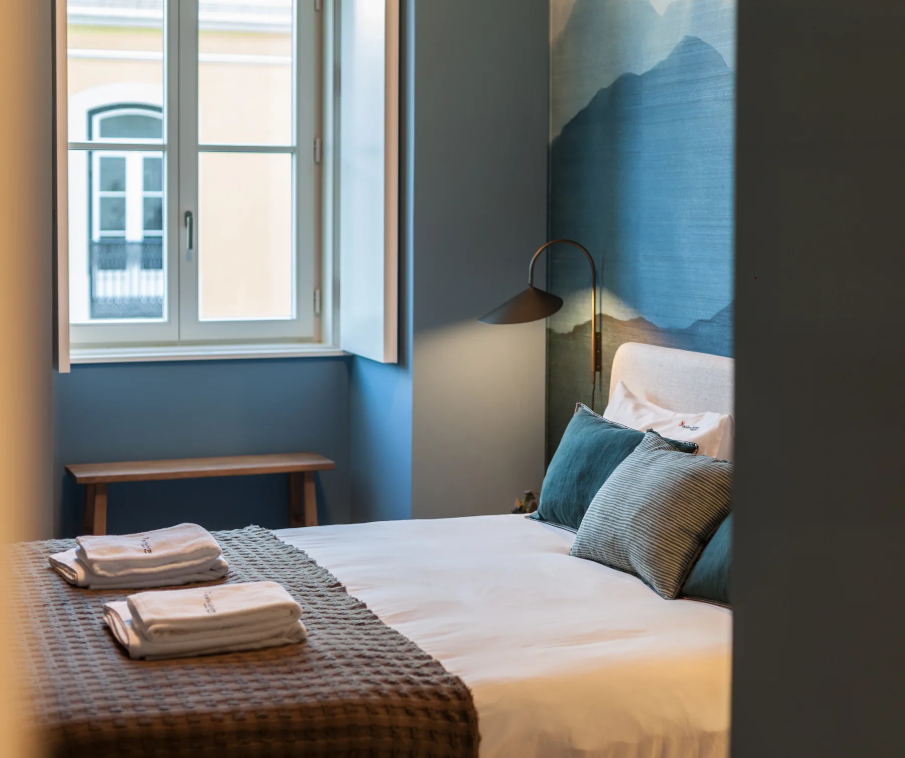 Un dormitorio con una cama, toallas dobladas y una ventana.