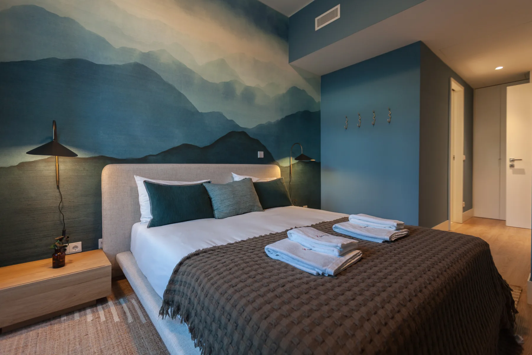 Un dormitorio con una cama bien hecha, toallas dobladas y un mural de montañas.