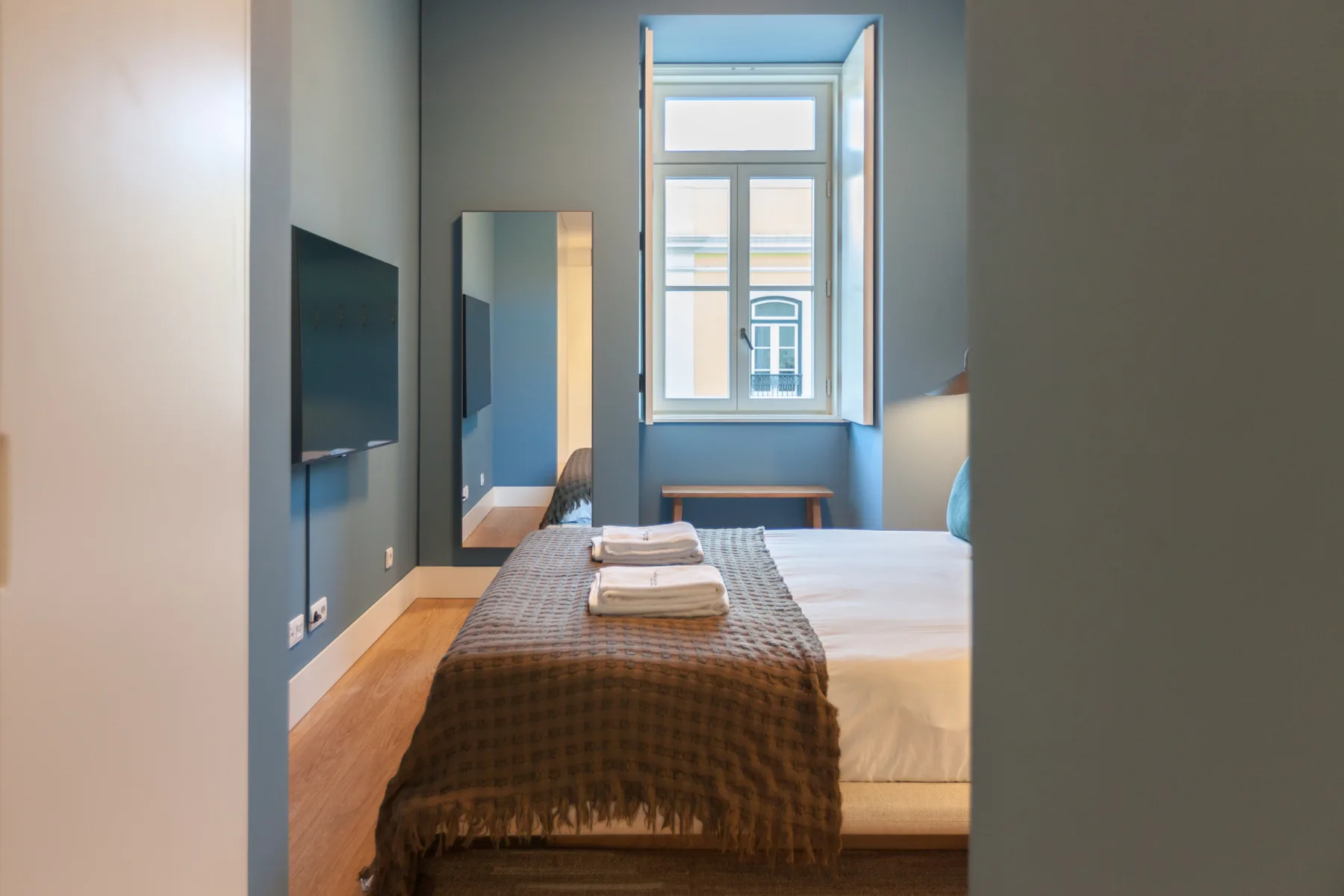 Un dormitorio con una cama bien arreglada, toallas dobladas y una ventana alta.