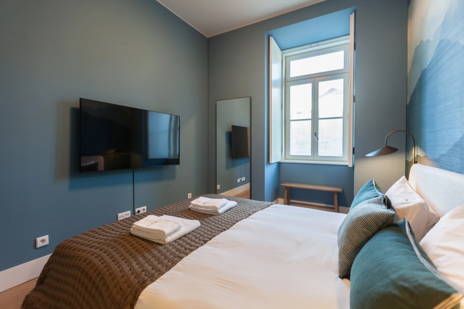 Un dormitorio con una cama bien hecha, toallas dobladas y un televisor en la pared.