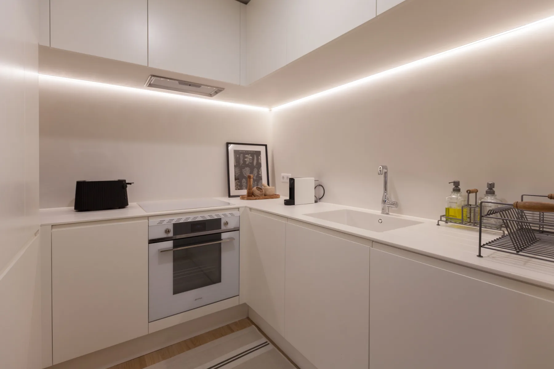 Una cocina moderna con armarios blancos, un horno integrado y un fregadero.