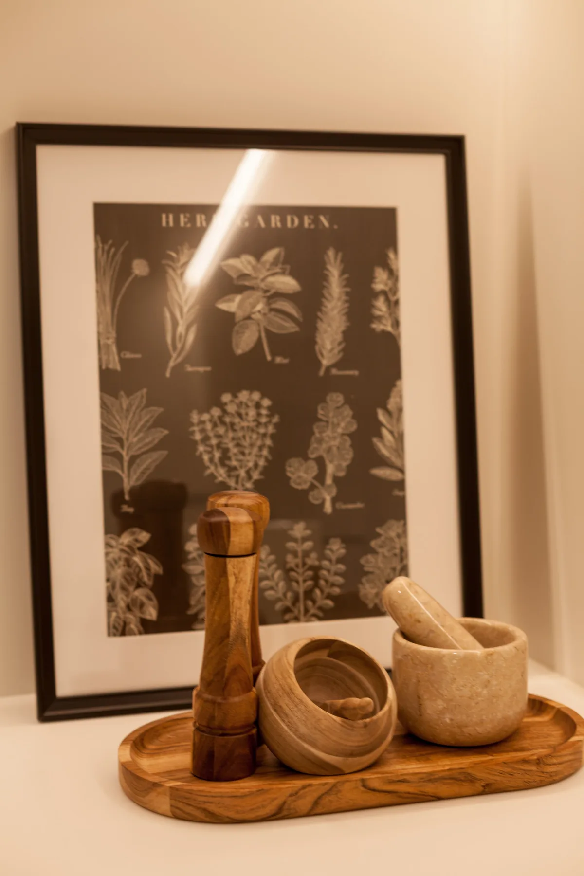Una ilustración enmarcada de hierbas está detrás de utensilios de madera y un cuenco de piedra sobre una bandeja.