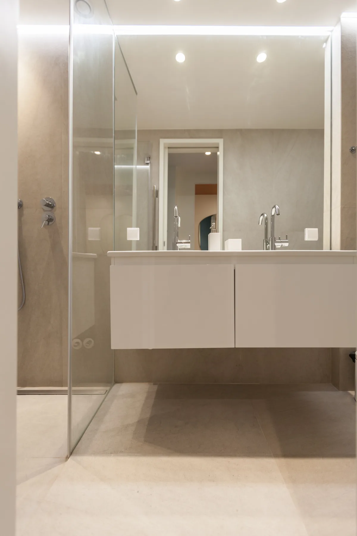 Un baño luminoso con una ducha de vidrio y un lavabo suspendido.