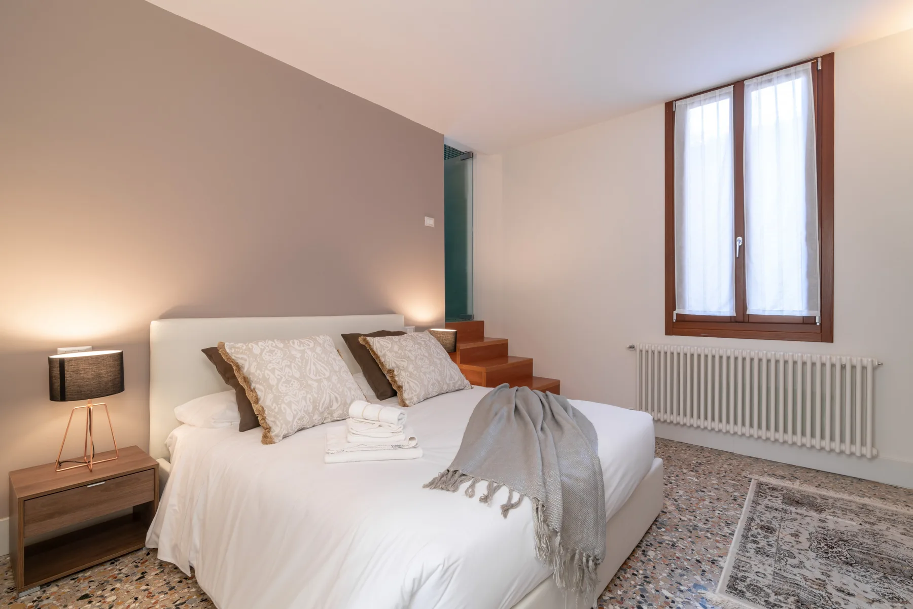 Un dormitorio con una cama bien hecha y una ventana sobre un radiador.